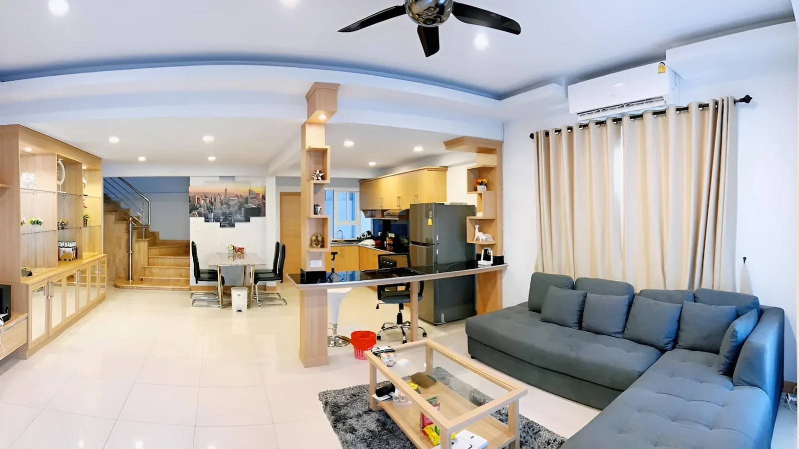 Open-plan living, kitchen and dining area of After Party Villas with grey sectional sofa and staircase